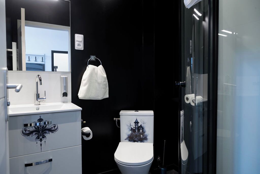 Un baño moderno con un lavamanos blanco, un inodoro de diseño gótico y una cabina de ducha de vidrio.
