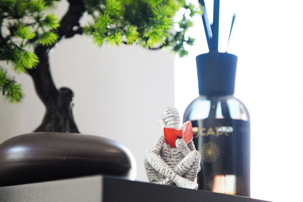 Un objet décoratif représentant une personne tenant un objet rouge, une bouteille noire avec du texte et un bonsaï.