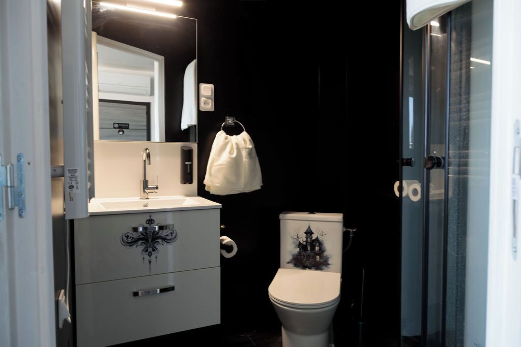 Un bagno con lavandino bianco, uno specchio, un WC decorato con una grafica di una casa infestata e una zona doccia.