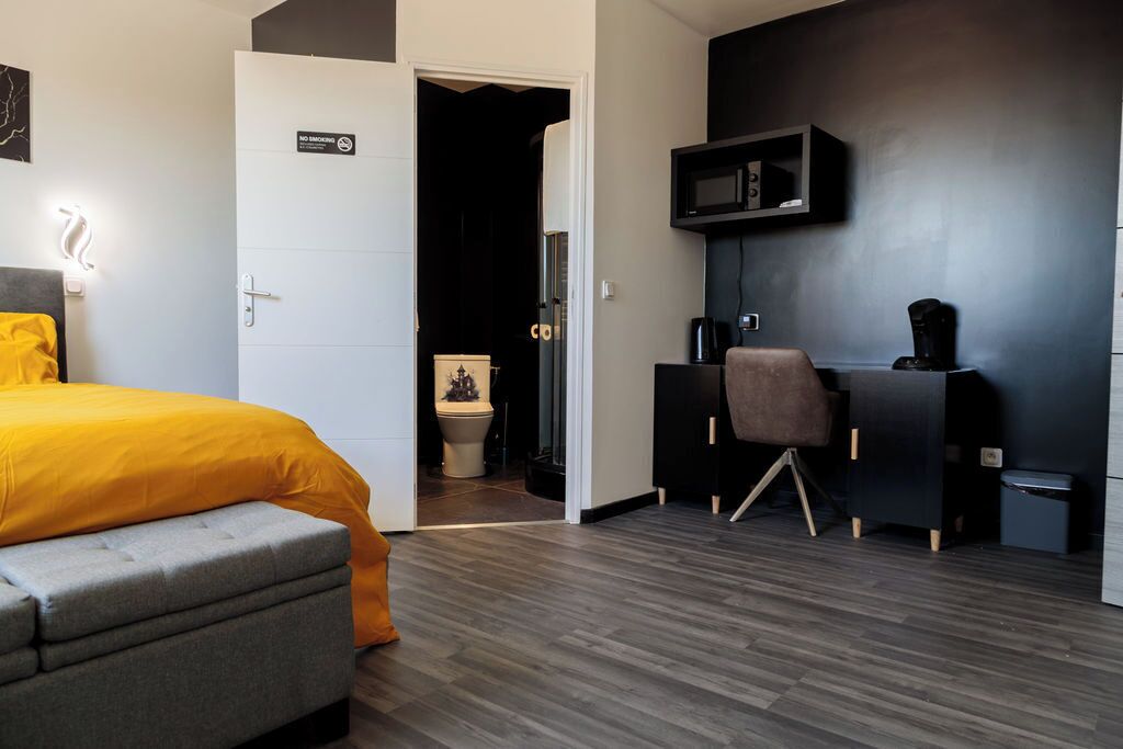 Una habitación de hotel moderna con una cama, un escritorio, una silla, un microondas y un pequeño cubo de basura.
