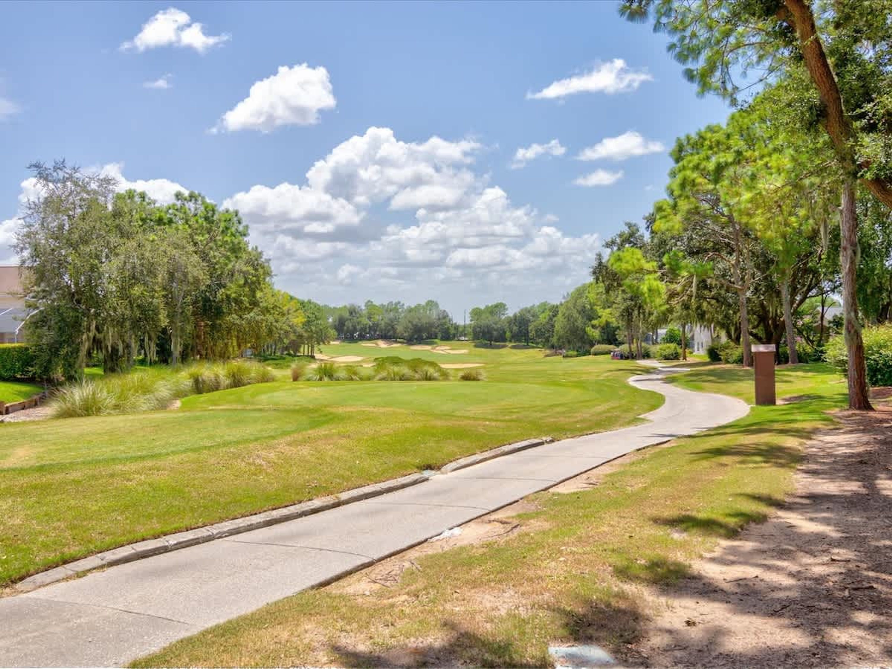 Ein Golfplatz mit befestigtem Weg, umgeben von Bäumen und Grün.
