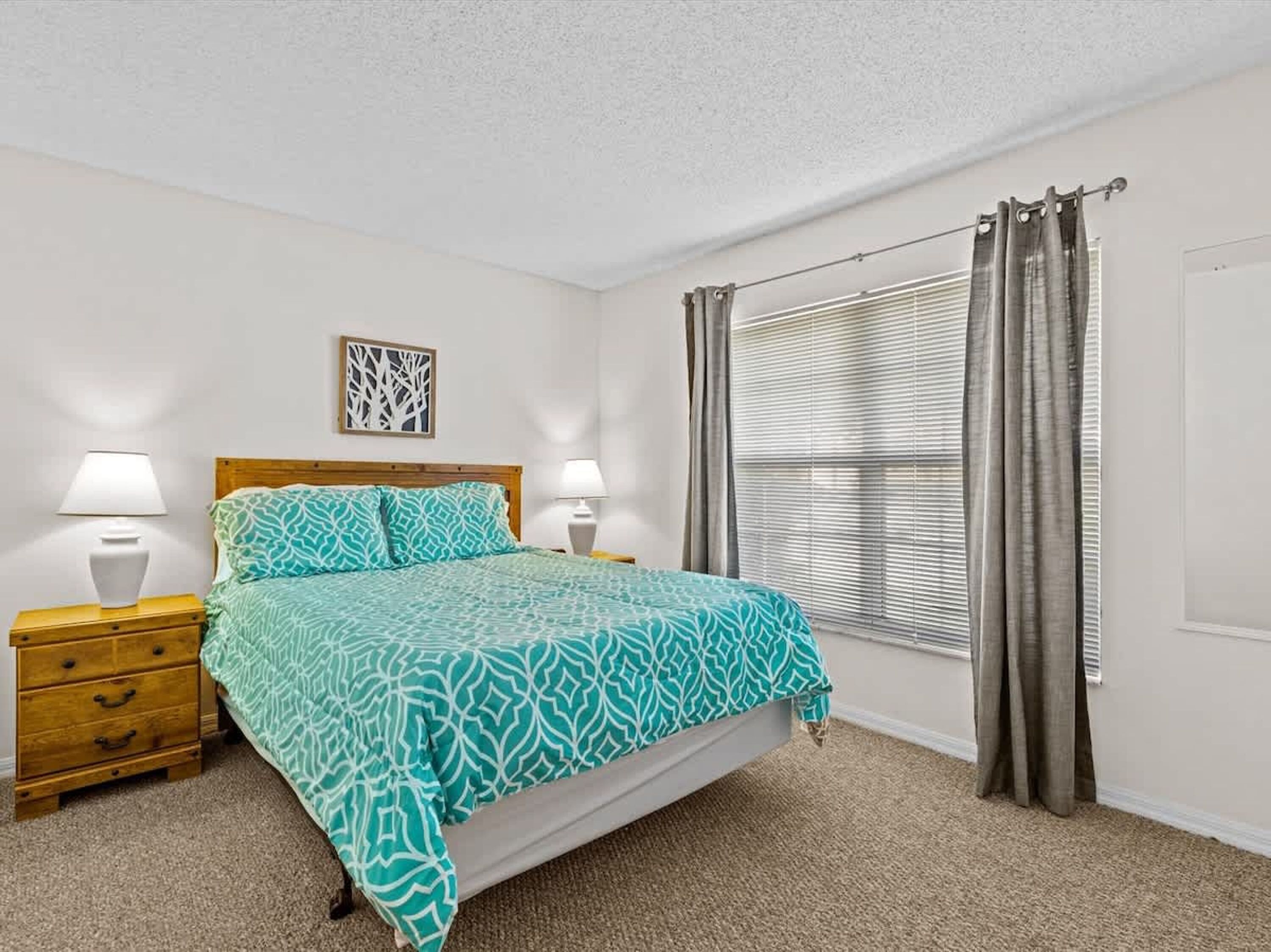 A bedroom with a bed, two bedside tables, a nightstand, a window with curtains, and a door.