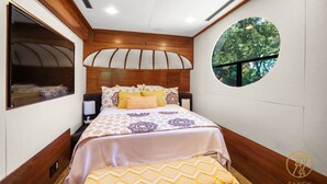 Une chambre avec un grand lit, une fenêtre donnant sur des arbres et une fenêtre ronde dans le mur.