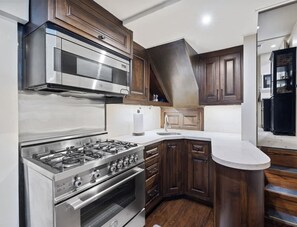 Una cocina moderna con electrodomésticos de acero inoxidable, gabinetes de madera oscura y encimera blanca.