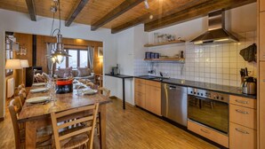 Una cocina moderna con vigas de madera, electrodomésticos de acero inoxidable y un comedor con mesa y sillas de madera.