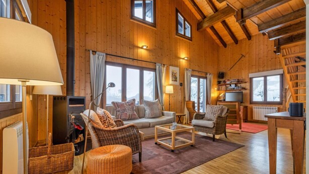 Interior acogedor de una cabaña de madera con un sofá, sillones de mimbre, una mesa de centro y una mesa de comedor.