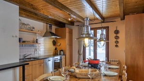 Una cocina con armarios de madera, un salpicadero de azulejos y una zona de comedor con una mesa de madera preparada para cuatro comensales.