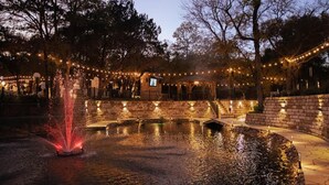 A nighttime outdoor area with a fountain, stone walls, and string lights. - The Heat 7744 Ranch Resort Austin Tx (Austin)