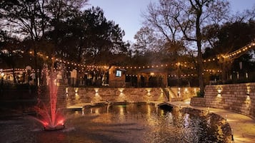 A nighttime outdoor area with a fountain, stone walls, and string lights.