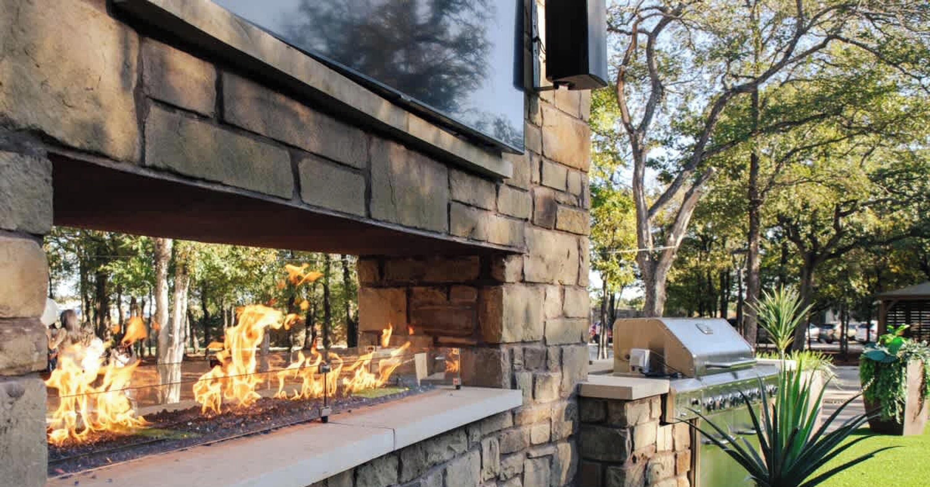 An outdoor stone wall with a built-in fire feature and a barbecue grill.