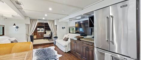 A modern kitchen with stainless steel appliances, a dining area with a zebra print rug, and a cozy seating area with a sofa and a TV.