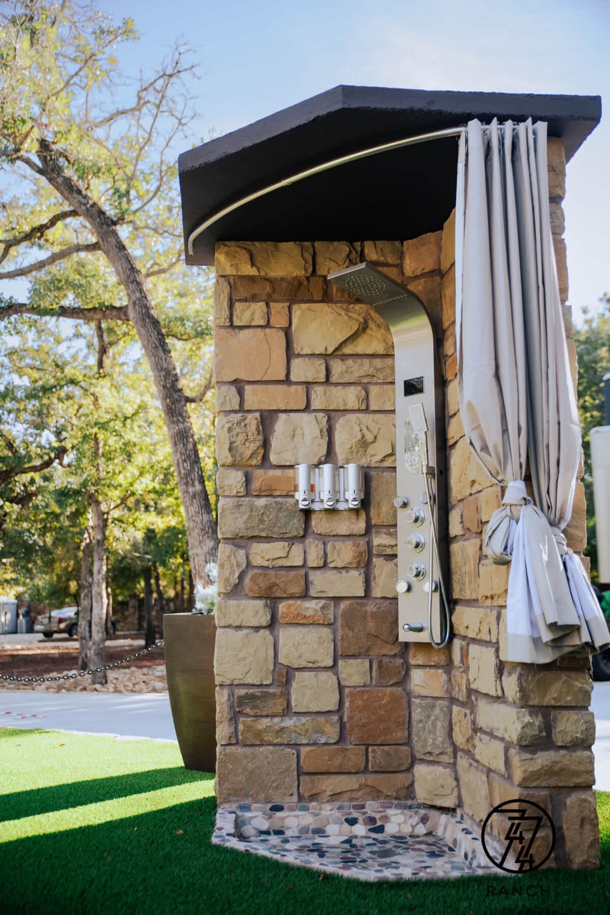 A stone-built outdoor shower with a curved showerhead and a towel hanging on the side.