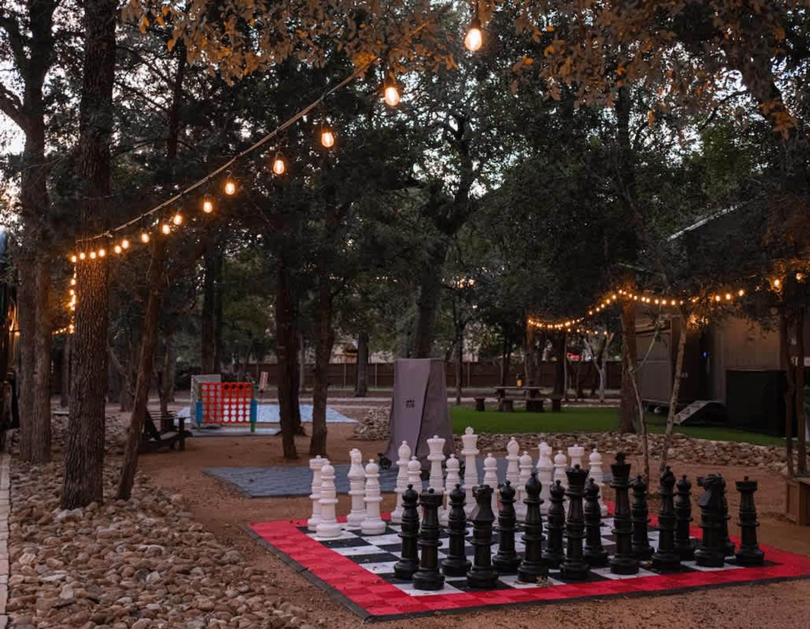 A chessboard set up outdoors with string lights overhead.