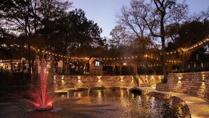 A nighttime outdoor area with a water feature, brick walls, and string lights. - The Aspen Unit in Austin (Austin)