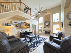 A spacious living room with a high ceiling, a fireplace, a television, and a staircase leading to an upper level.