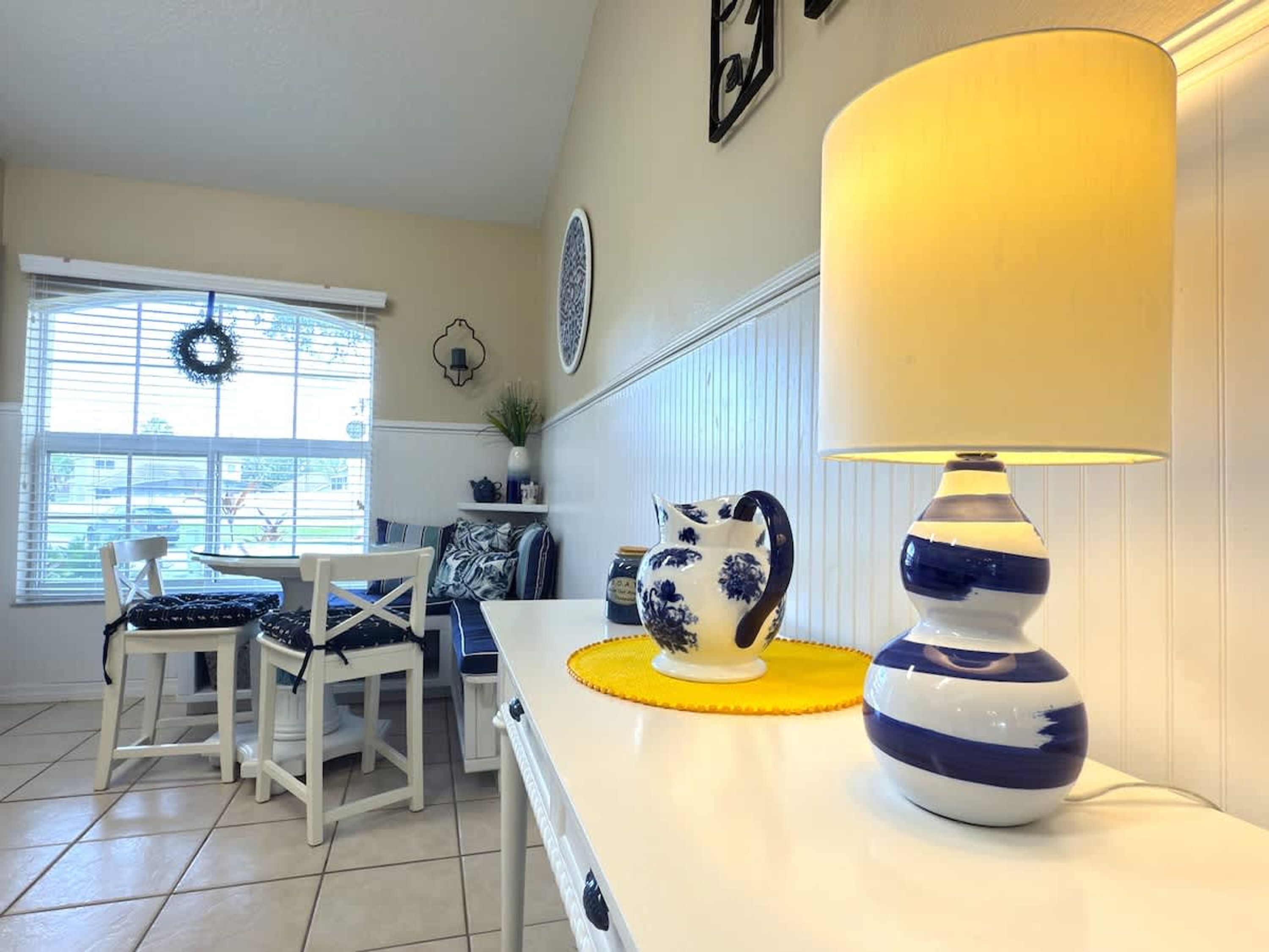 A kitchen with a dining area, featuring a white countertop, a blue and white lamp, and a decorative pitcher.