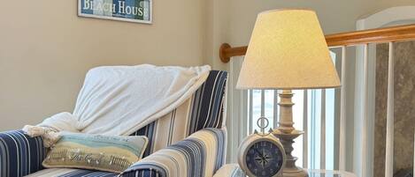 Una habitación con sillones a rayas, una mesa con una lámpara, un reloj y un letrero enmarcado en la pared.