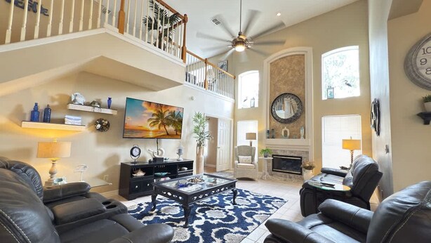 A spacious living room with a high ceiling, a large TV, leather sofas, a fireplace, and a staircase leading to an upper level. - Near Disney Villa 3 bd Private Pool (Davenport)