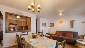 A dining area with a table set for four, a sofa, and a kitchen in the background. - Nevada 205 4 pax Central Apartment Garage (Riddes)