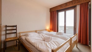 A hotel room with two wooden beds, a chair, a window with curtains, and a view of the outside. - Nevada 205 4 pax Central Apartment Garage (Riddes)
