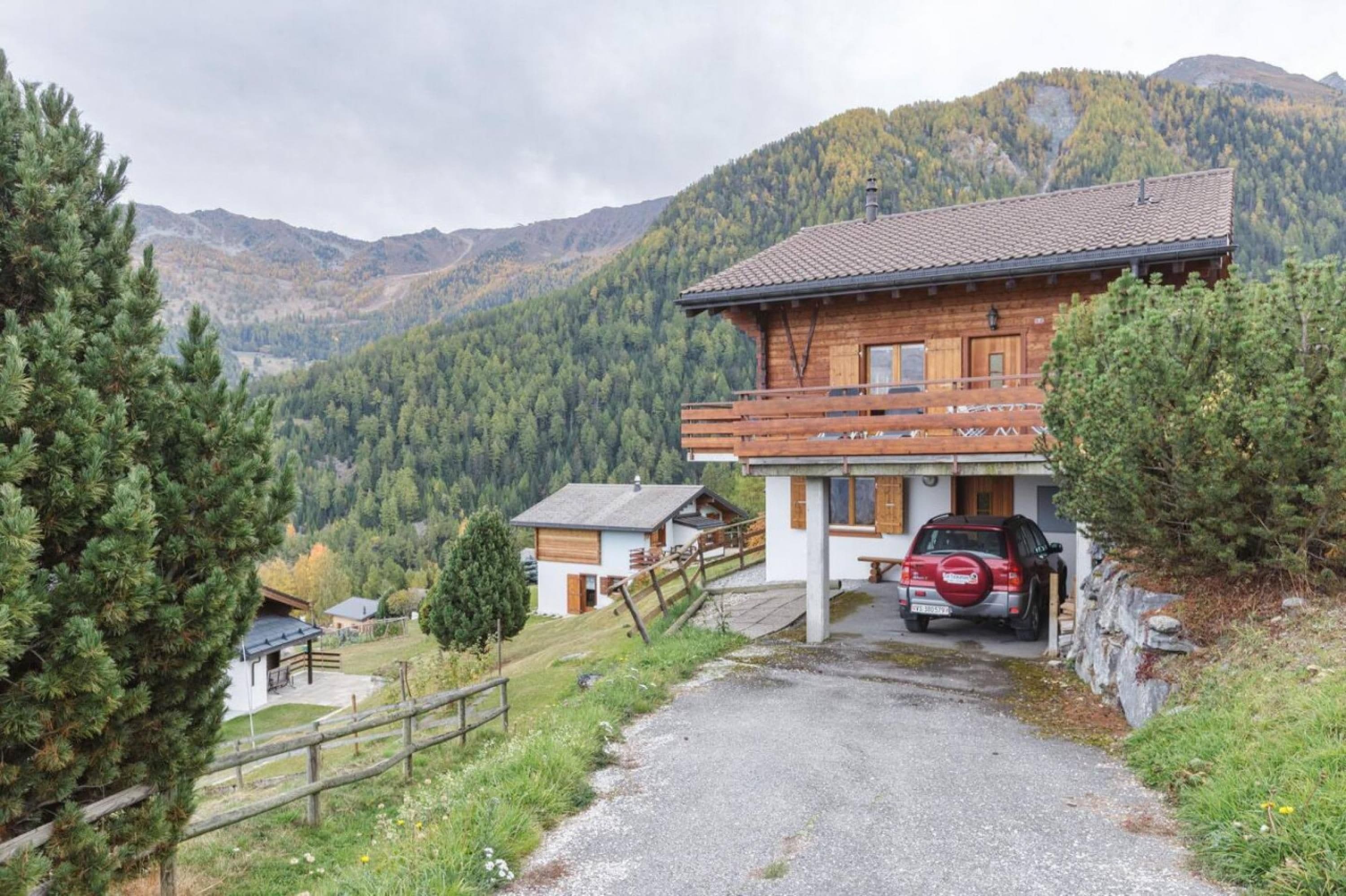 Una baita in legno con vialetto sterrato, immersa tra pini e montagne.