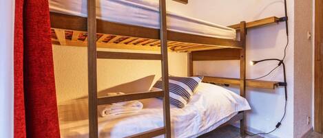A bunk bed with a wooden frame, a white mattress, and a striped pillow. There is a red curtain partially visible on the left.