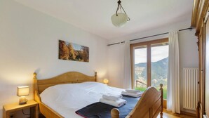 A wooden bed with white linens, a bedside lamp, and a view of a mountainous landscape through a window. - El Paradiso - Luxury Chalet Sauna w Views (Riddes)