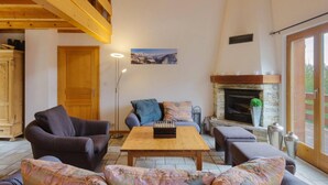 A cozy living room with a fireplace, wooden beams, and a large window. - El Paradiso - Luxury Chalet Sauna w Views (Riddes)
