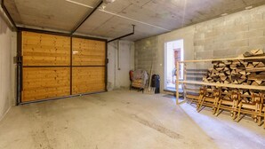 Un garage con porta in legno, pavimento in cemento e una pila di legna.