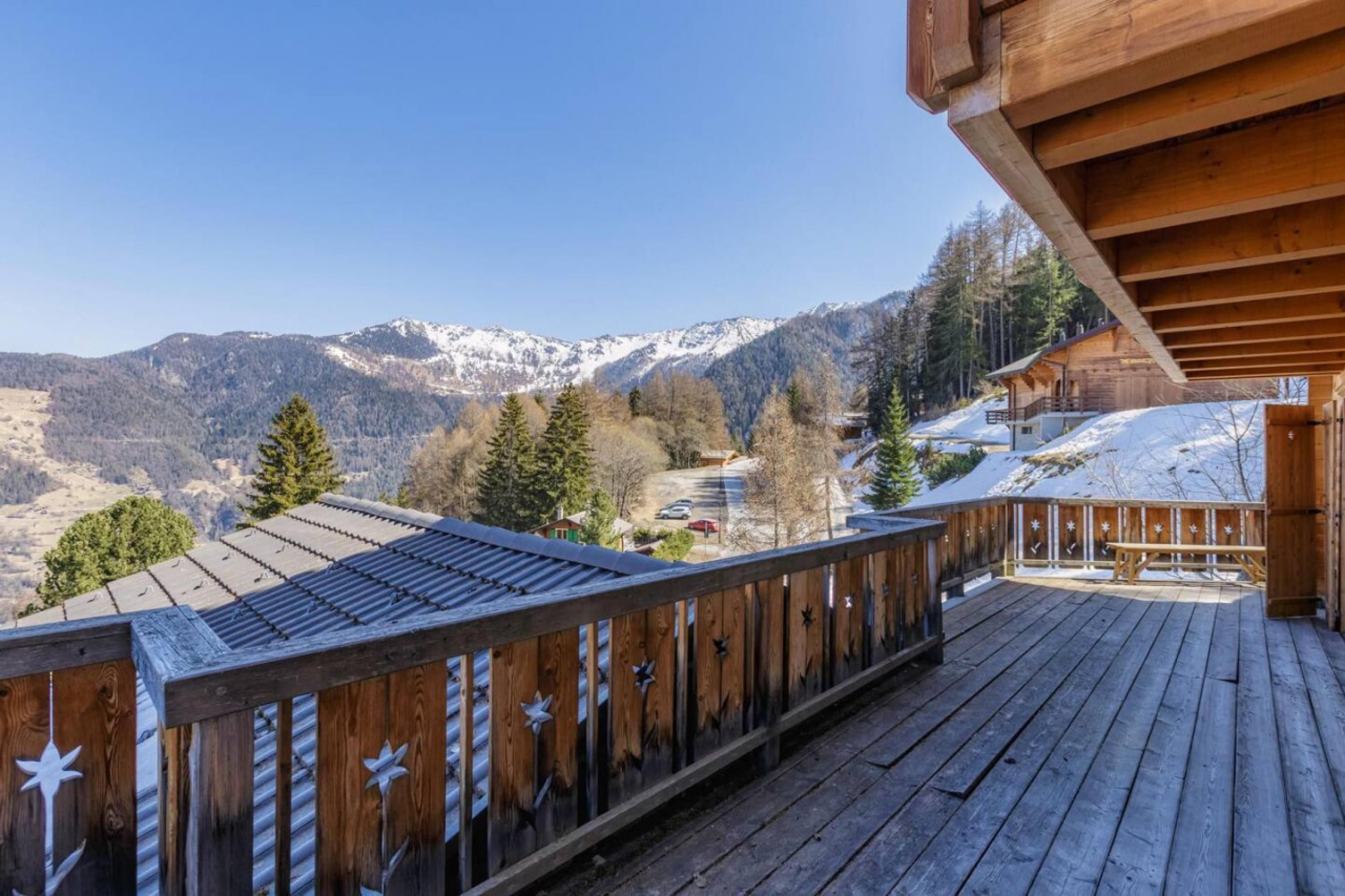 Une terrasse en bois offrant une vue sur des montagnes enneigées et un ciel dégagé.