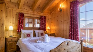 Una camera da letto in stile baita con un letto, due lampade ai comodini, una finestra con tende e vista sull'esterno.