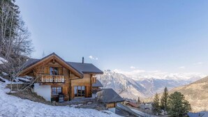 Un chalet in legno con un balcone, circondato da montagne innevate e cieli tersi.