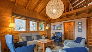 A cozy log cabin interior with a wooden ceiling, a large woven light fixture, a sofa, chairs, and a coffee table. - Chalet Elbaz - Swiss Chalet With Breathtaking Views (Riddes)