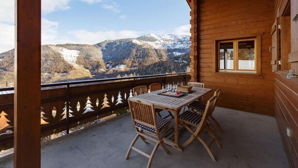 A wooden balcony with a table and chairs, overlooking a mountainous landscape with snow-capped peaks. - Chalet Elbaz - Swiss Chalet With Breathtaking Views (Riddes)