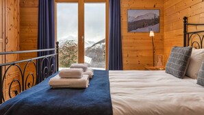 A wooden cabin bedroom with a bed, towels, a lamp, and a mountain view. - Chalet Elbaz - Swiss Chalet With Breathtaking Views (Riddes)