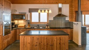A modern kitchen with wooden cabinets, a central island, a stove, and a large window. - Chalet Elbaz - Swiss Chalet With Breathtaking Views (Riddes)