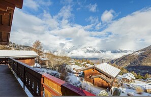 Una cabaña de madera con balcón que da a un pueblo montañoso cubierto de nieve.