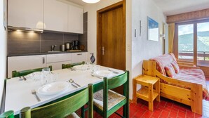A cozy room with a wooden bed, a dining table set with plates and glasses, and a kitchen with white cabinets and a wooden door. - Belle Vue Apartment 423 (Riddes)