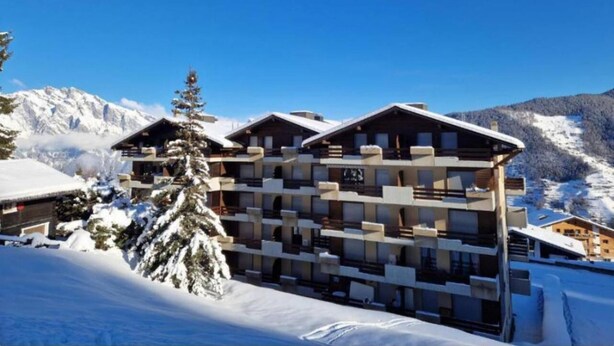 A multi-story hotel with a modern architectural design, featuring balconies and a snowy mountain backdrop. - Belle Vue Apartment 423 (Riddes)