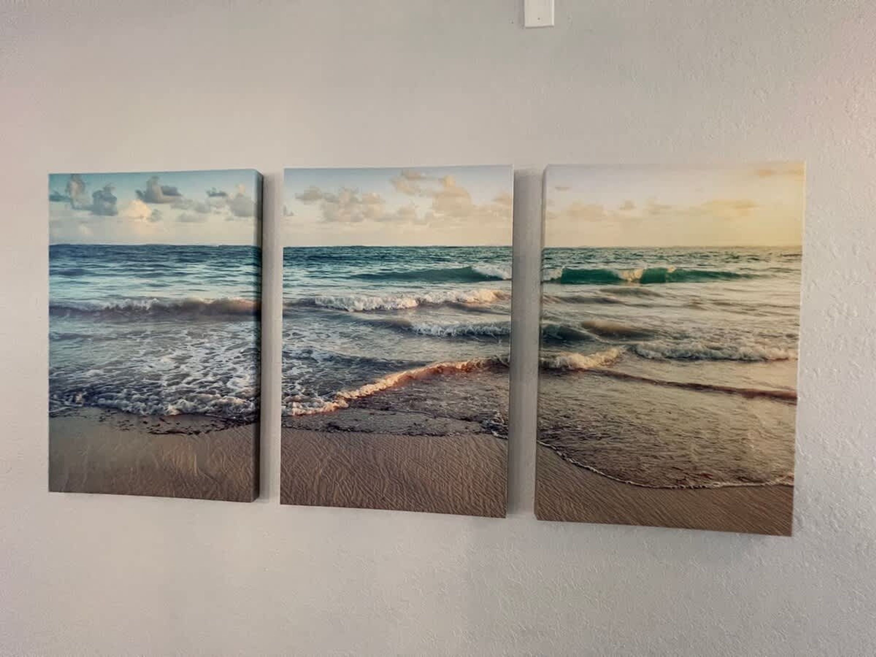 Un triptyque mural représentant une scène de plage, avec des vagues et un ciel nuageux.