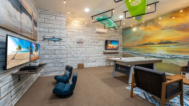 A room with a white brick wall, a mounted TV, a surfboard, and a beach mural. - Wildlife Themed Villa 4 Bd Pool Near Disney (Davenport)