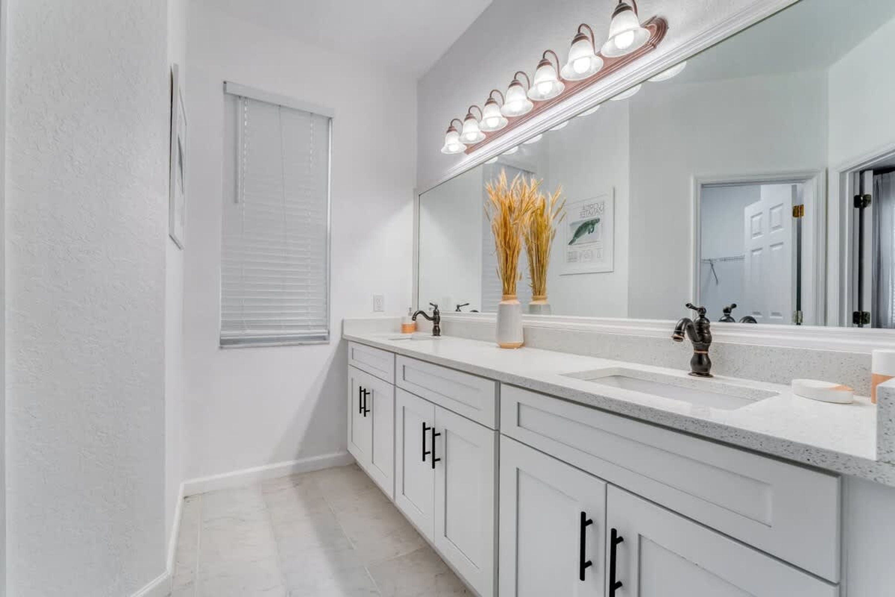 A bathroom with a double sink vanity, a large mirror, and a light fixture above the mirror.