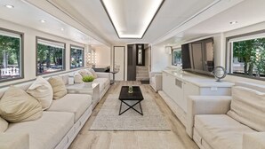 A modern living room with a sofa, coffee table, and a TV. There are large windows and a staircase leading to another level. - Studio 7744 Ranch Austin Venue and Rentals (Austin)