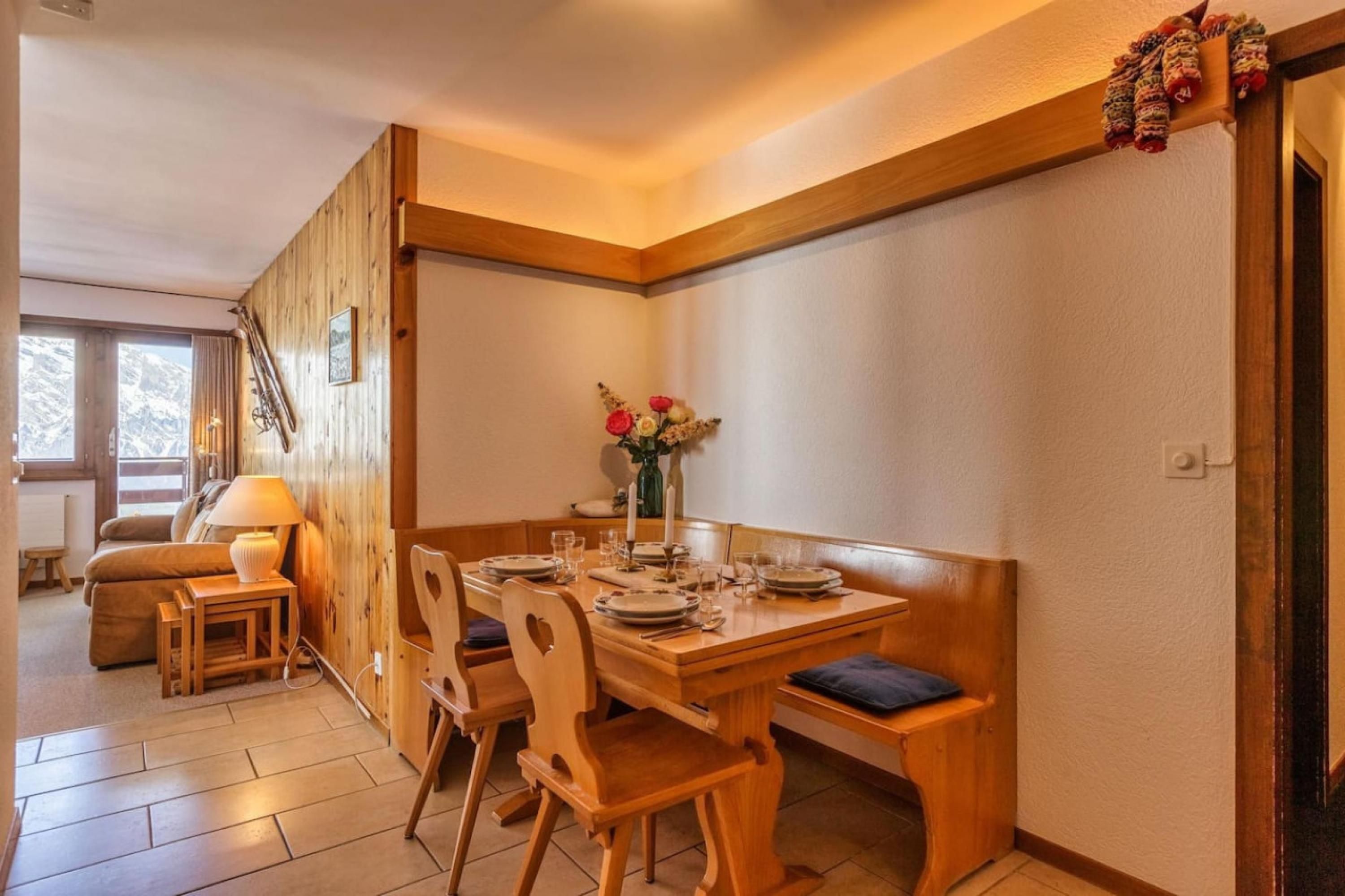 A dining area with wooden furniture, a table set for four, and a vase with flowers on the table.