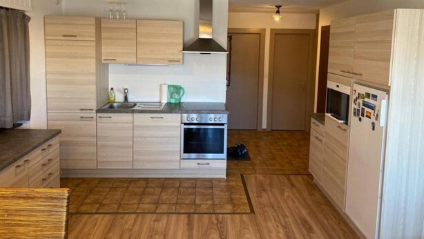 Een compacte keuken met lichte houten kastjes, een roestvrijstalen oven en een ingebouwde magnetron. Twee hanglampen en een raam boven de spoelbak.