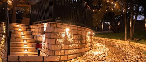 A stone retaining wall with a water feature, a wooden deck, and string lights.