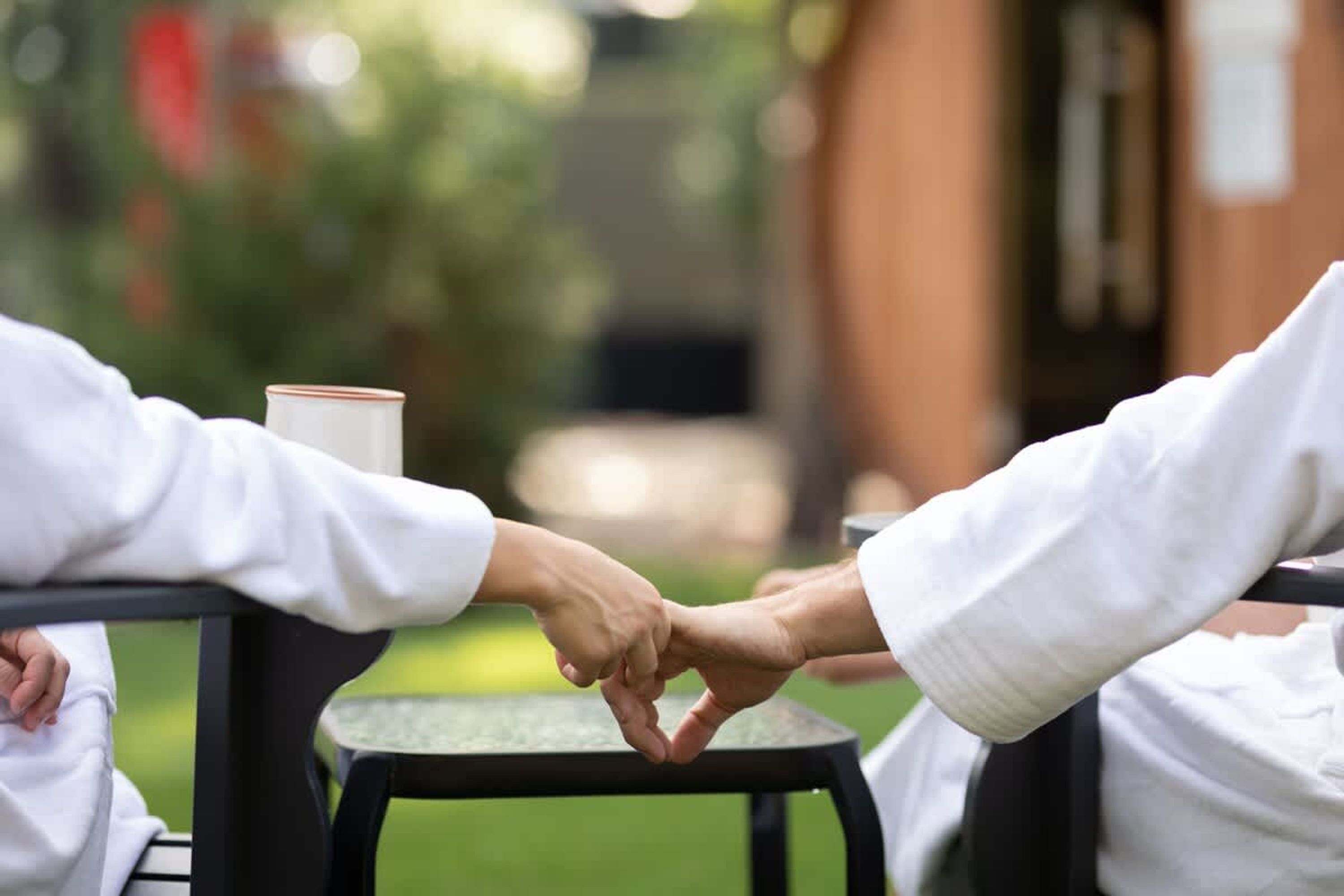 Two people holding hands at a table with a cup.