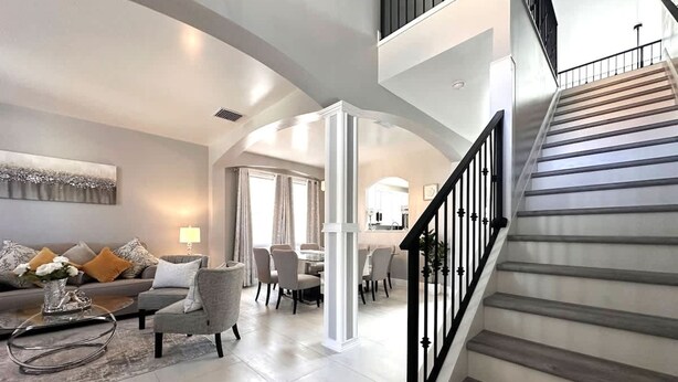 A spacious living area with a modern staircase, a dining area, and a kitchen in the background.