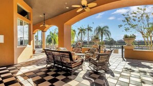 A covered outdoor seating area with checkered flooring, wicker furniture, and a view of palm trees and buildings.