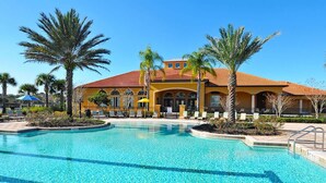 A hotel with a swimming pool, palm trees, and a yellow building with a red roof.